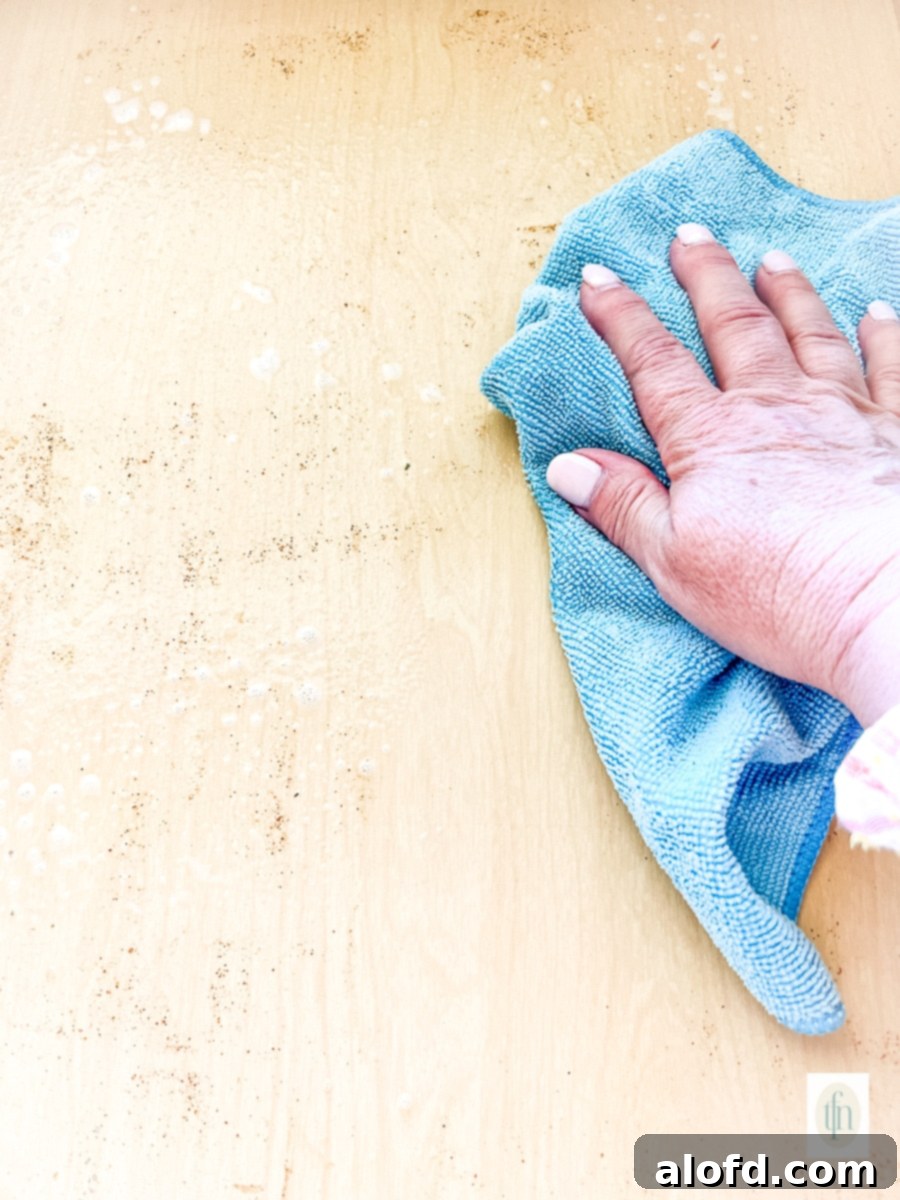 Using a microfiber cloth and food safe cleaner to wipe out the inside of a dirty spice drawer.