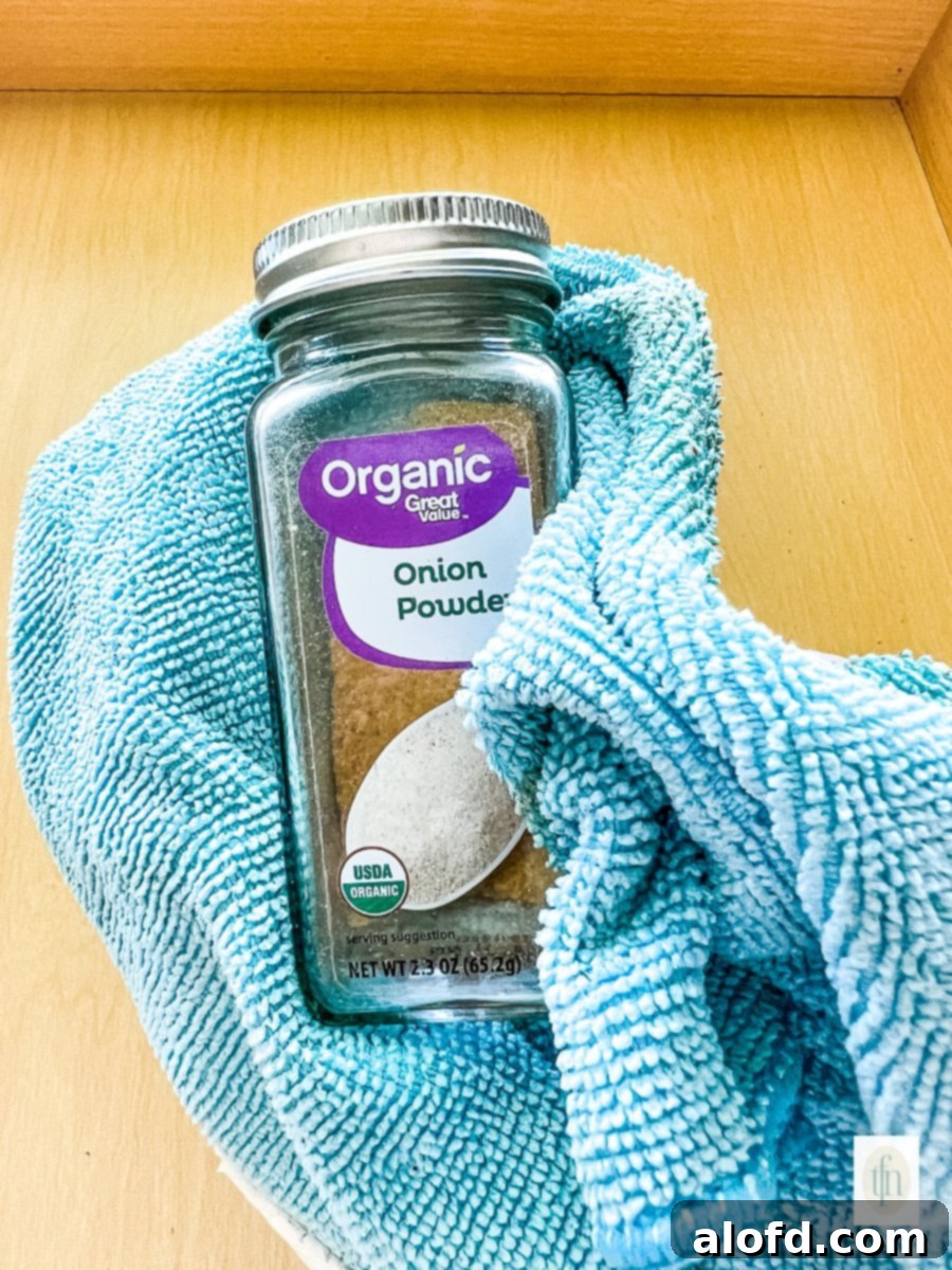 Cleaning a glass jar of onion powder with a blue microfiber cloth.