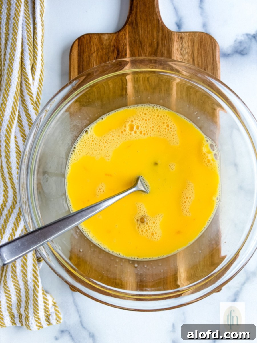 Tangy Sourdough Morning Stack 5 Fork in a clear glass mixing bowl with yellow liquid, representing whisked eggs.