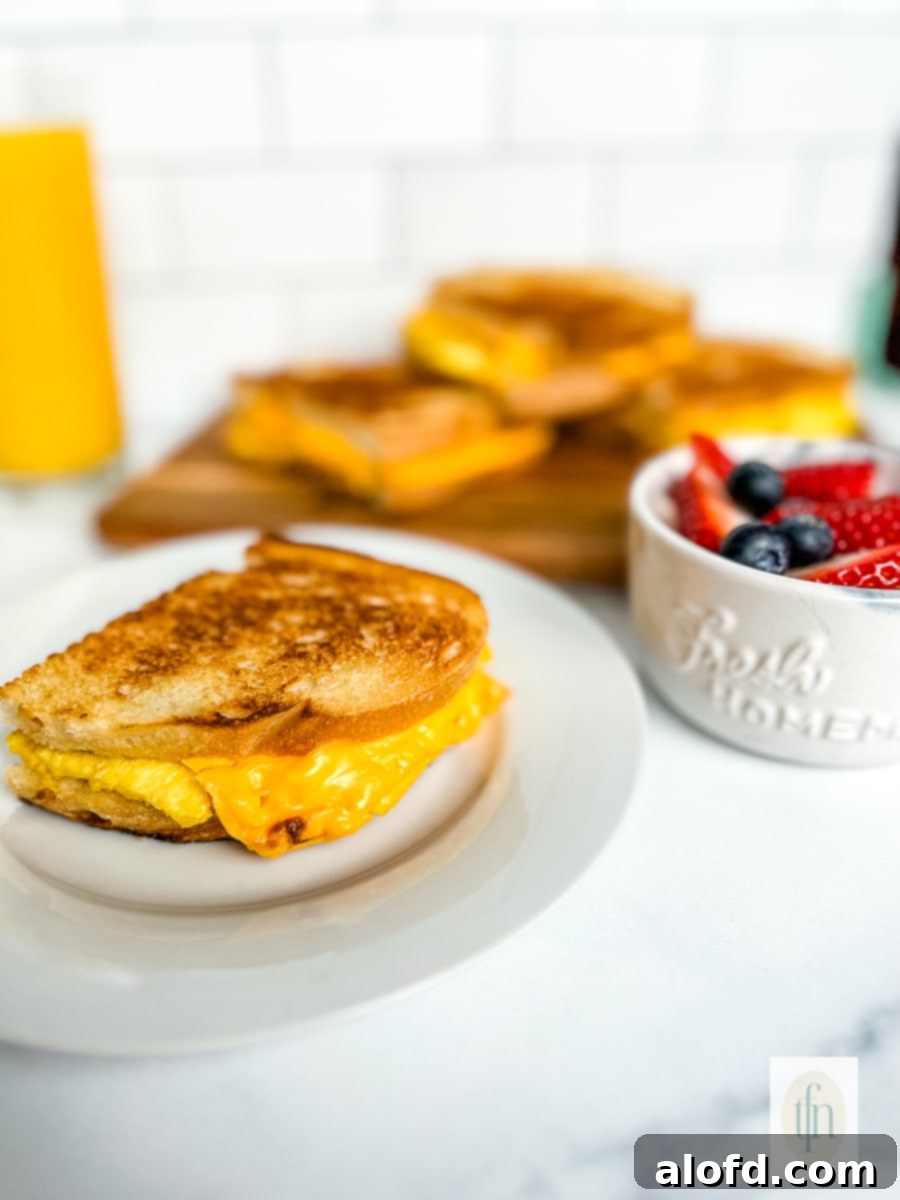 Tangy Sourdough Morning Stack 10 Grilled scrambled egg sandwich on a plate next to a bowl with fresh blueberries and strawberries, creating a vibrant breakfast scene.