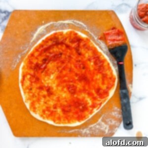 Ultimate Neapolitan Pizza Dough 8 San Marzano sauce brushed onto a pizza crust.