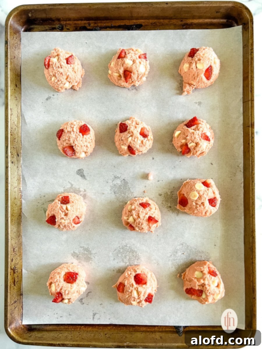Strawberry Cheesecake Cookie Bliss 9 Unbaked strawberry cheesecake cookies arranged on a rimmed baking sheet lined with parchment paper, spaced for optimal baking.