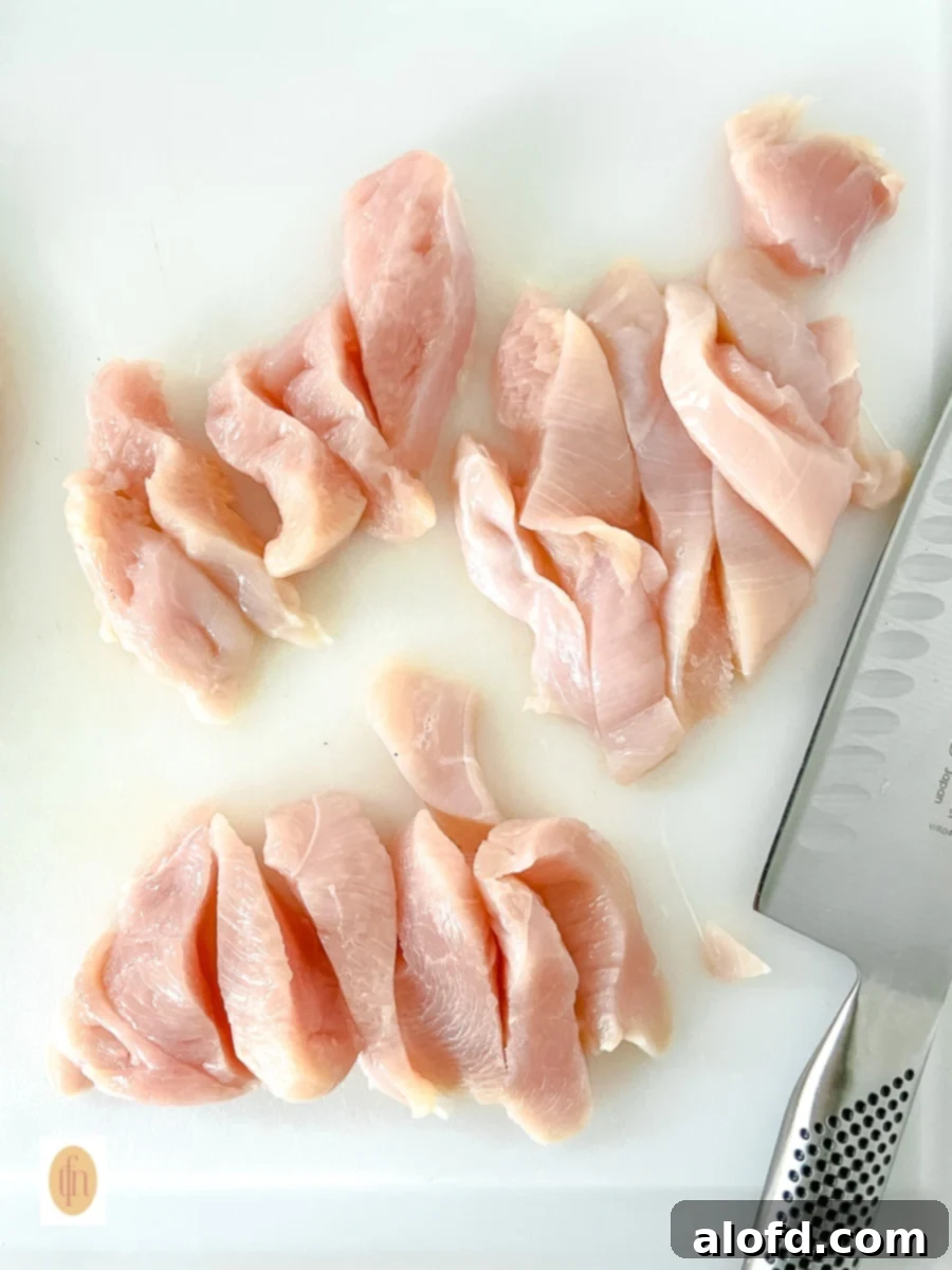 Chicken breast cut into strips on a cutting board.