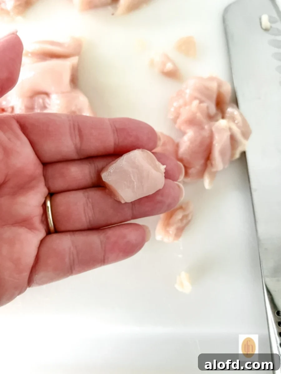 Chicken breast cut into cubes in a woman's hand, shown close up.