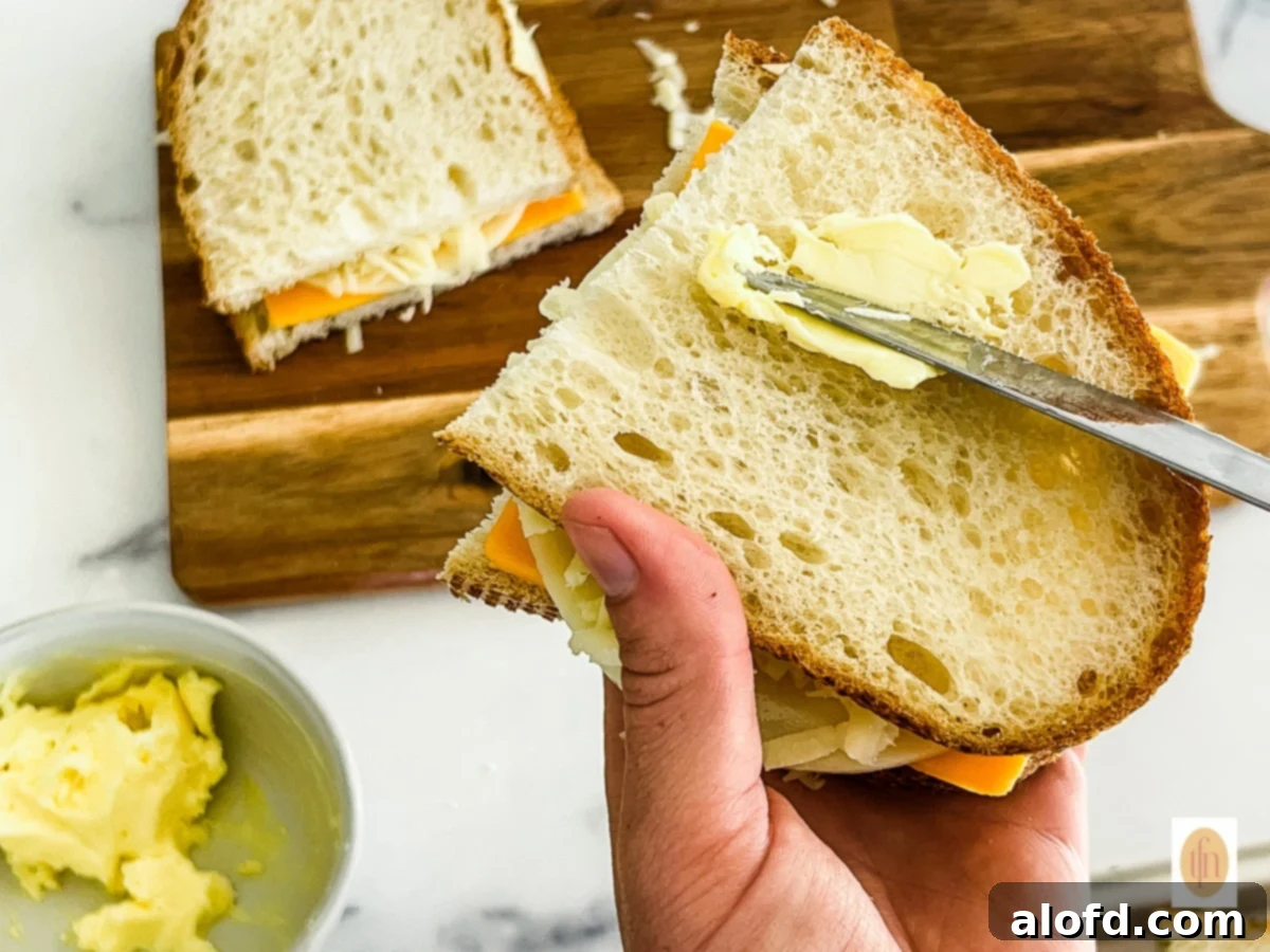 Tangy Sourdough Golden Cheese Melt 5 Buttering a slice of sourdough bread before assembling the grilled cheese sandwich on a griddle.