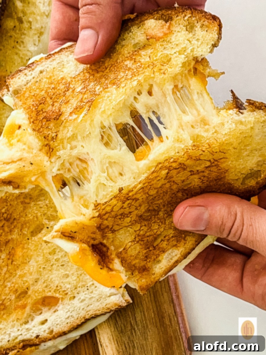 Tangy Sourdough Golden Cheese Melt 7 Man's hands pulling apart two halves of a melted cheese sourdough sandwich, showcasing the gooey, stretchy cheese.