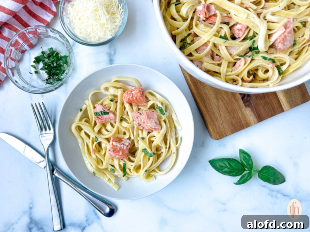 Decadent Salmon Alfredo 3 An individual serving of salmon alfredo pasta next to a larger bowl filled with the creamy dish, garnished with fresh herbs.