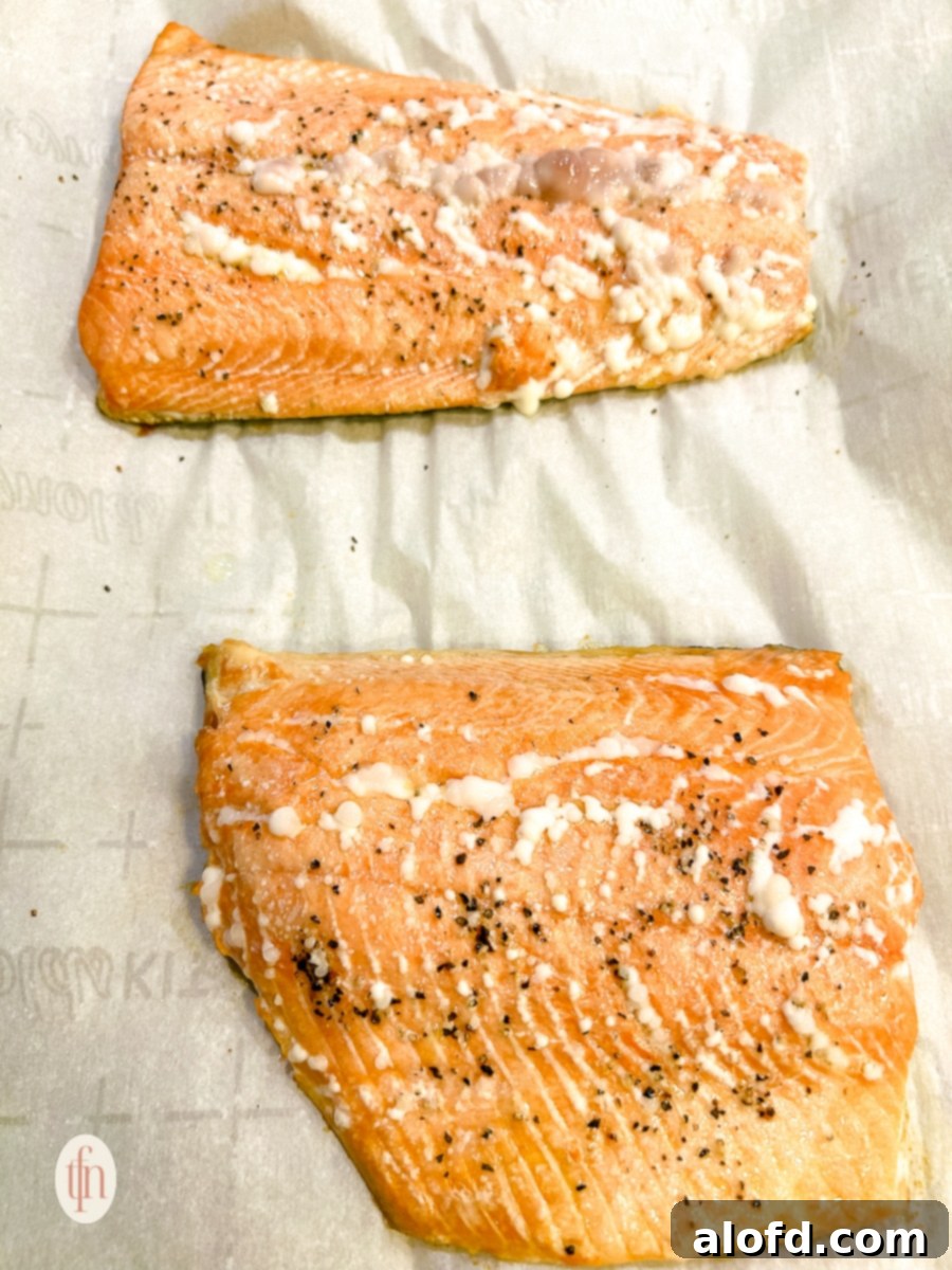 Decadent Salmon Alfredo 5 Two perfectly baked salmon fillets resting on parchment paper on a baking sheet, ready to be flaked for the Alfredo.