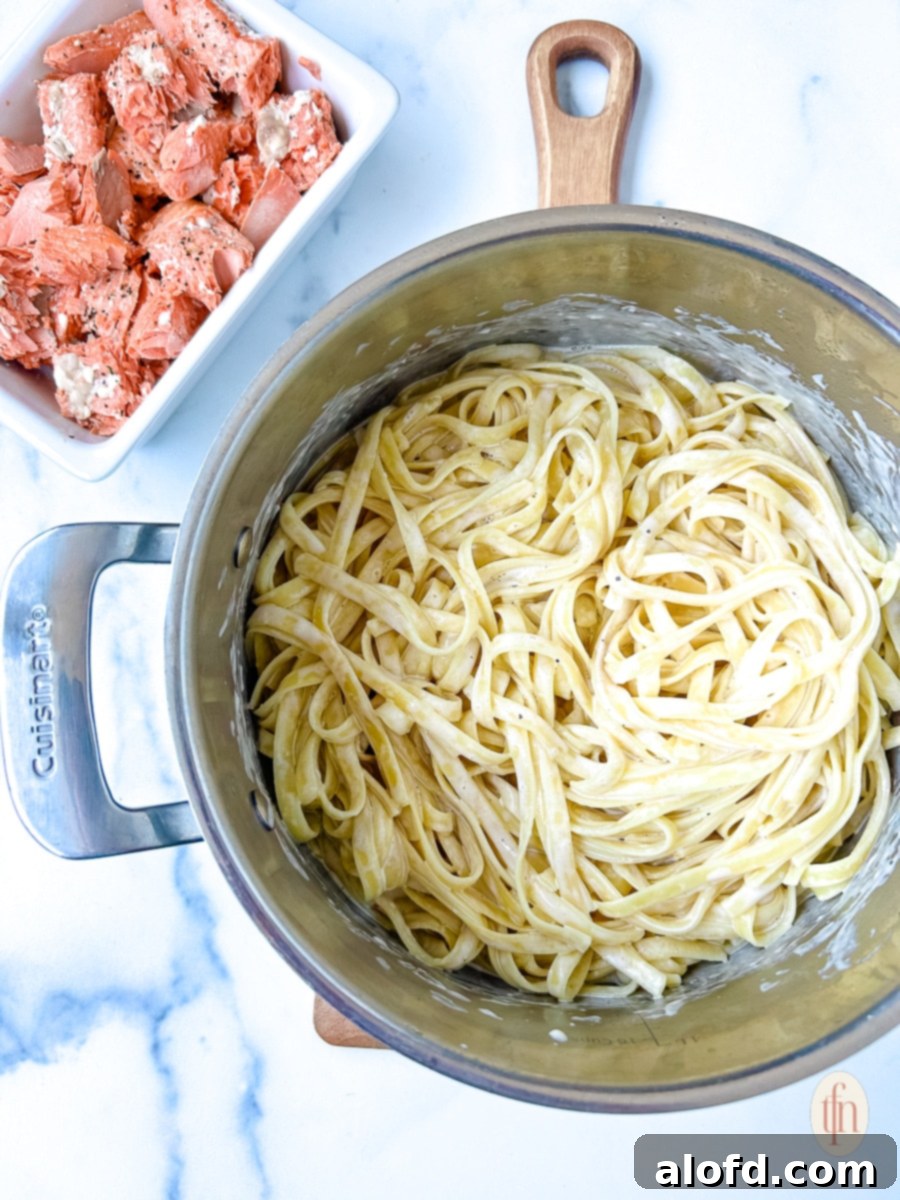 Decadent Salmon Alfredo 7 A dish of perfectly baked salmon fillets sitting adjacent to a pot of fettuccine pasta coated in creamy white Alfredo sauce.