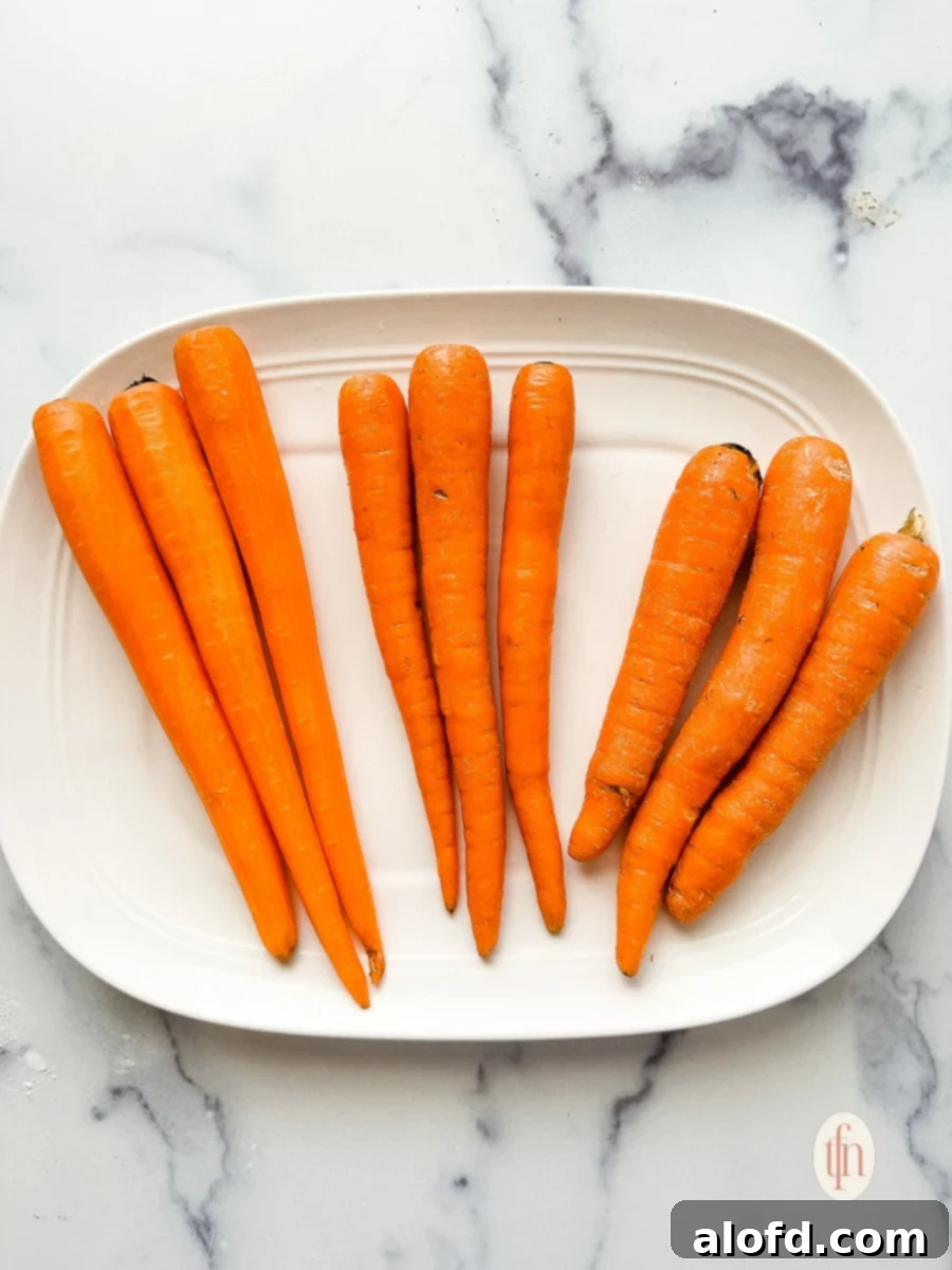 Nine long, thin, orange root vegetables on a white serving plate. Three of them have been peeled.