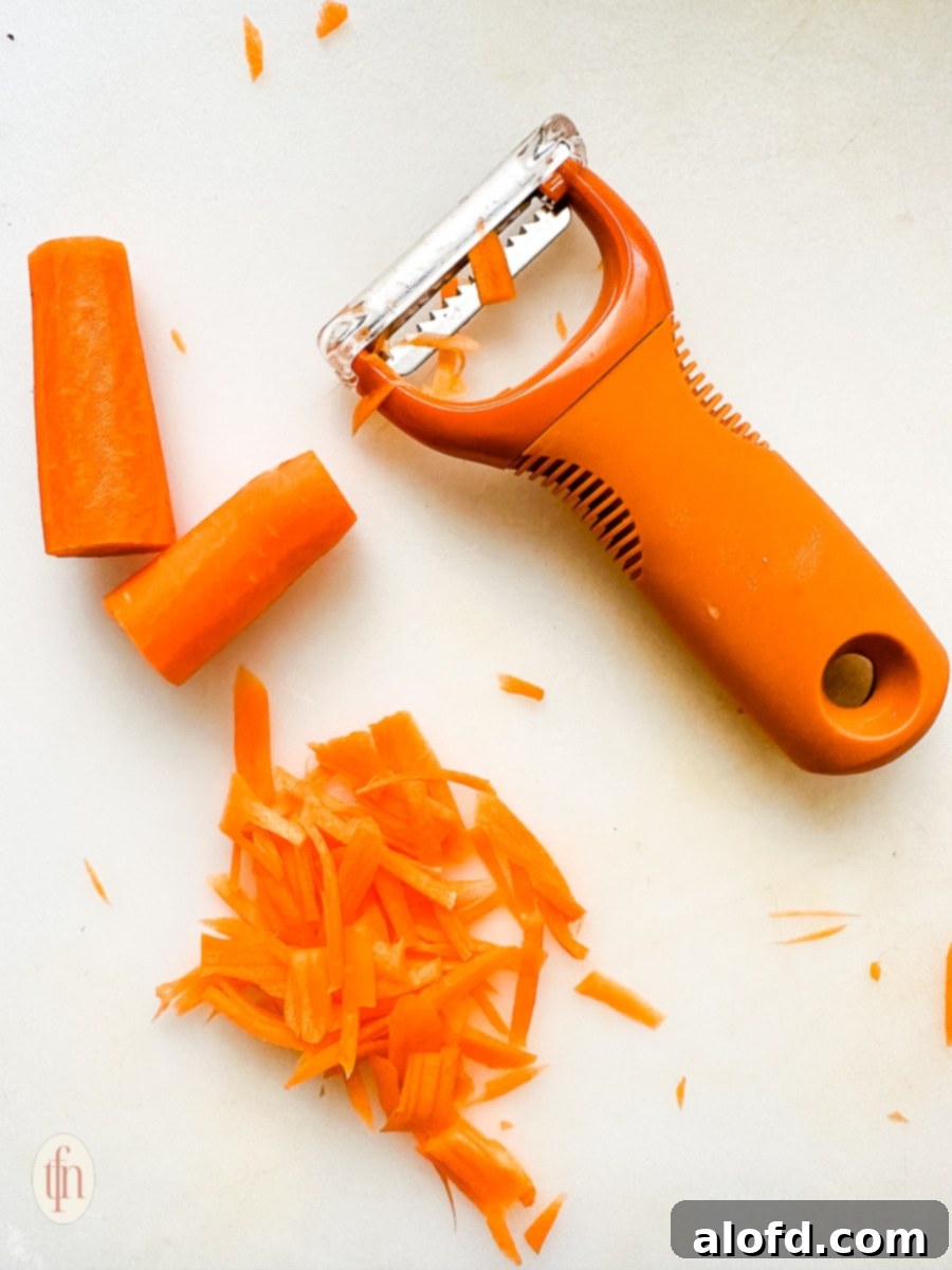 Shredded carrots next to a vegetable peeler.