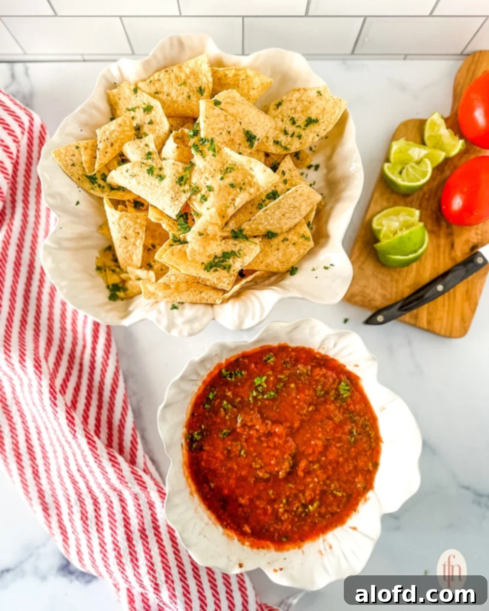 Food processor salsa in a serving bowl next to a basket filled with corn tortilla chips, ready to be served at a party or potluck.