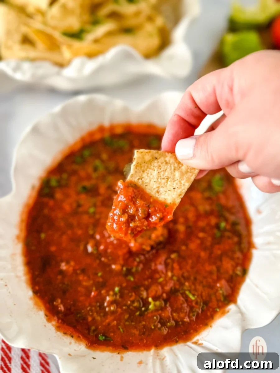 Close-up of a corn tortilla chip being dipped into a bowl of thick and chunky homemade jalapeño salsa, highlighting its appetizing texture.