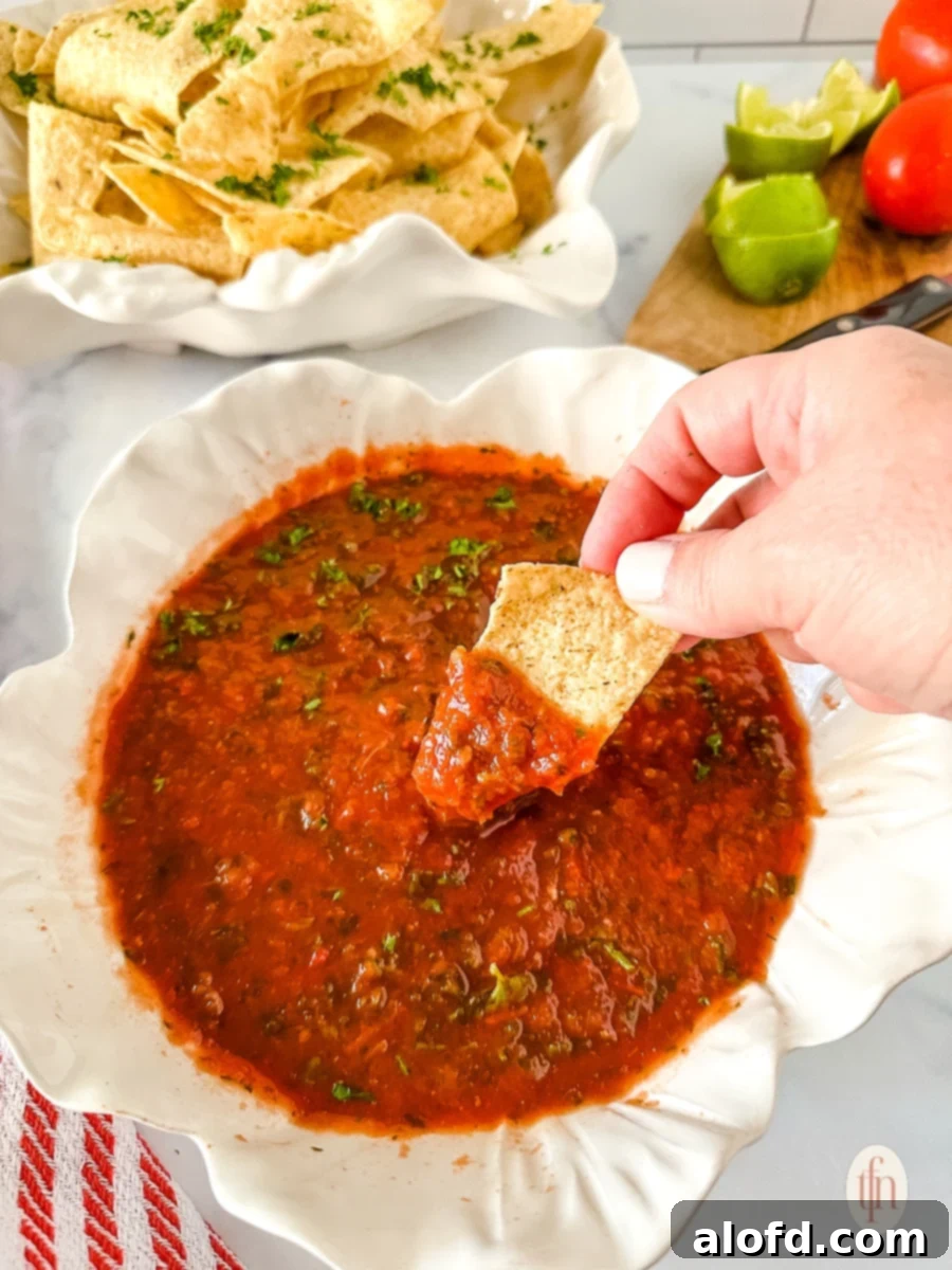 Dipping a crispy corn tortilla chip into a generously filled bowl of fresh, homemade jalapeño salsa, showcasing its vibrant texture.