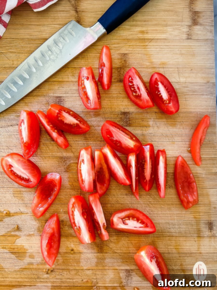 Precisely quartered Roma tomatoes laid out on a clean cutting board next to a chef's knife, demonstrating careful preparation for salsa making.