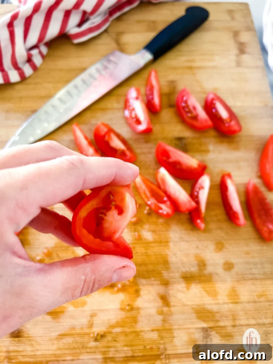 A hand gently squeezing chopped Roma tomatoes to remove excess juices, a technique for making thicker salsa.