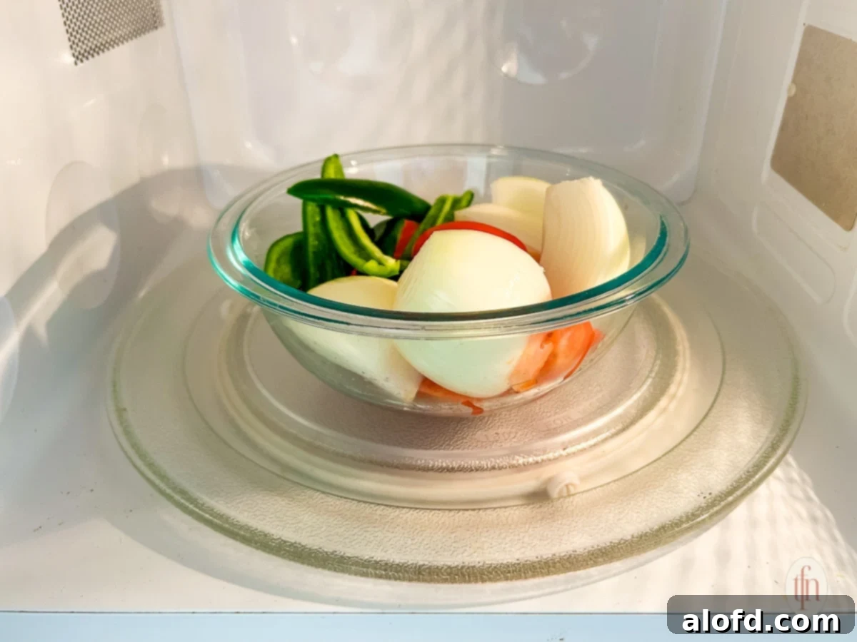 A clear glass bowl filled with chopped tomatoes, onions, and green chiles, ready to be microwaved for food processor salsa.