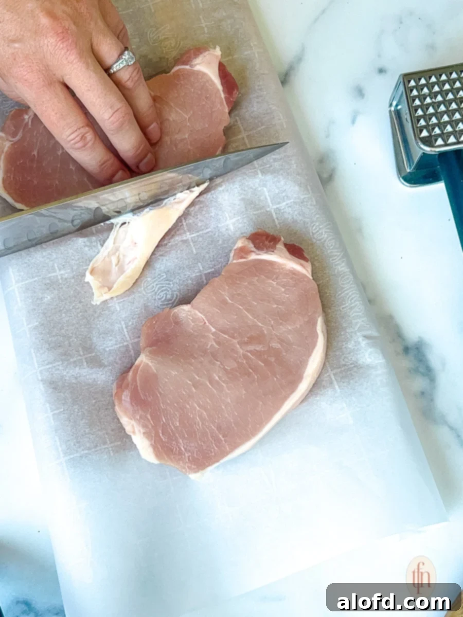 A person meticulously trimming excess fat from a piece of raw pork, demonstrating proper meat preparation techniques.