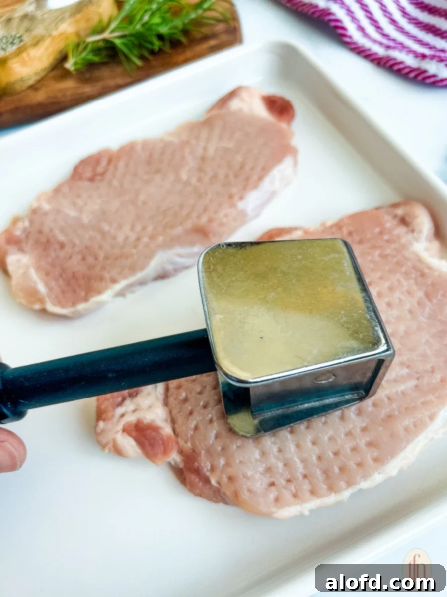 A woman's hands expertly demonstrating how to tenderize a raw pork chop using a meat tenderizing mallet on a cutting board.