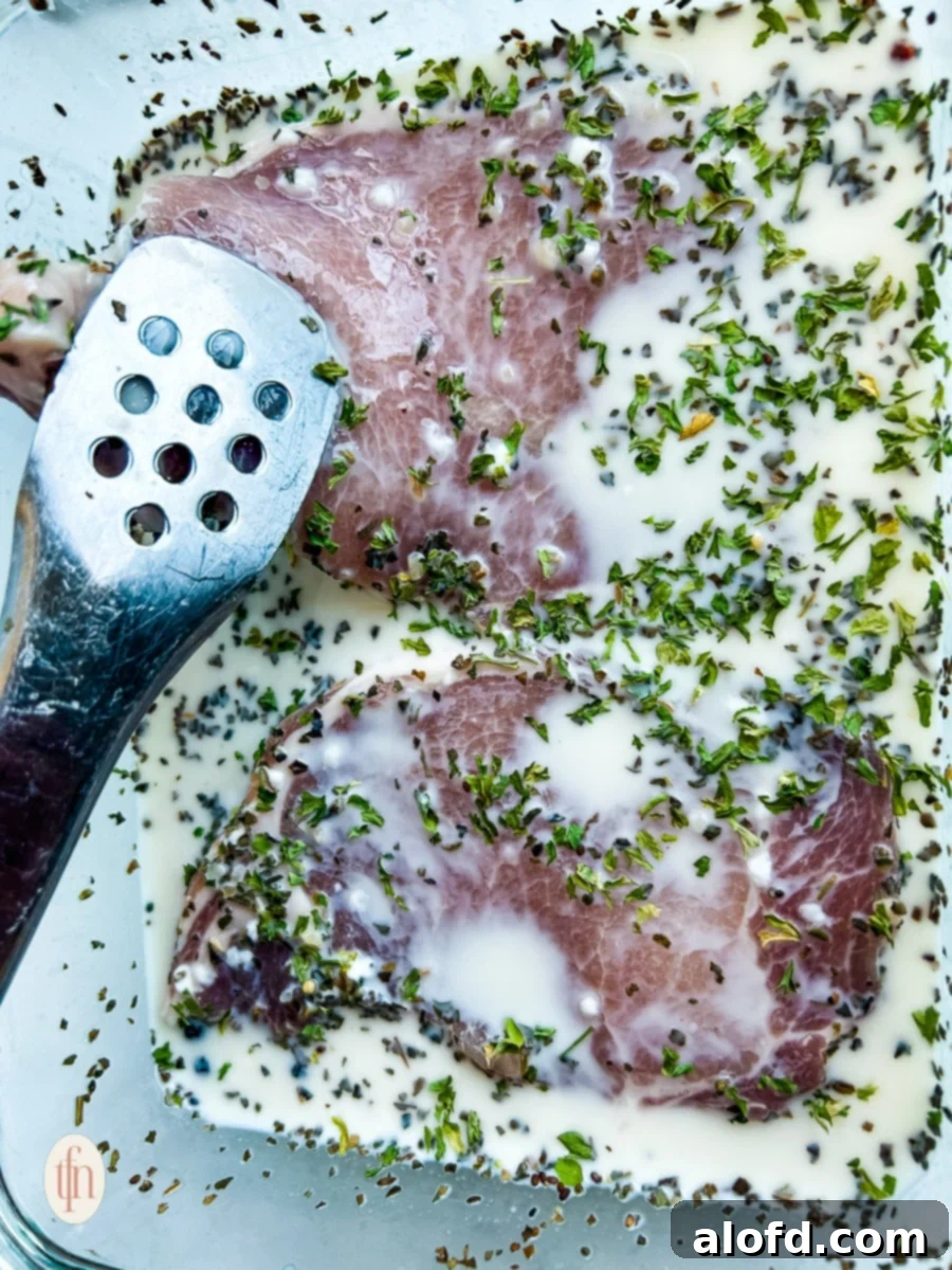 Two uncooked pork chops soaking in a flavorful brine solution within a glass bowl, ready for tenderizing.