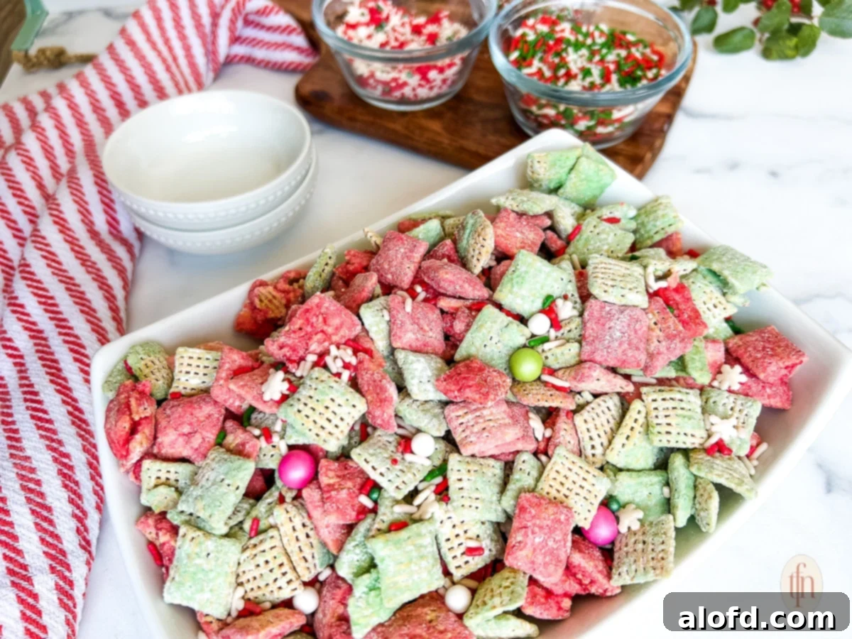 Festive Muddy Buddies 11 Large white dish containing Christmas muddy buddies next to smaller bowls filled with sprinkles on a white marble countertop.