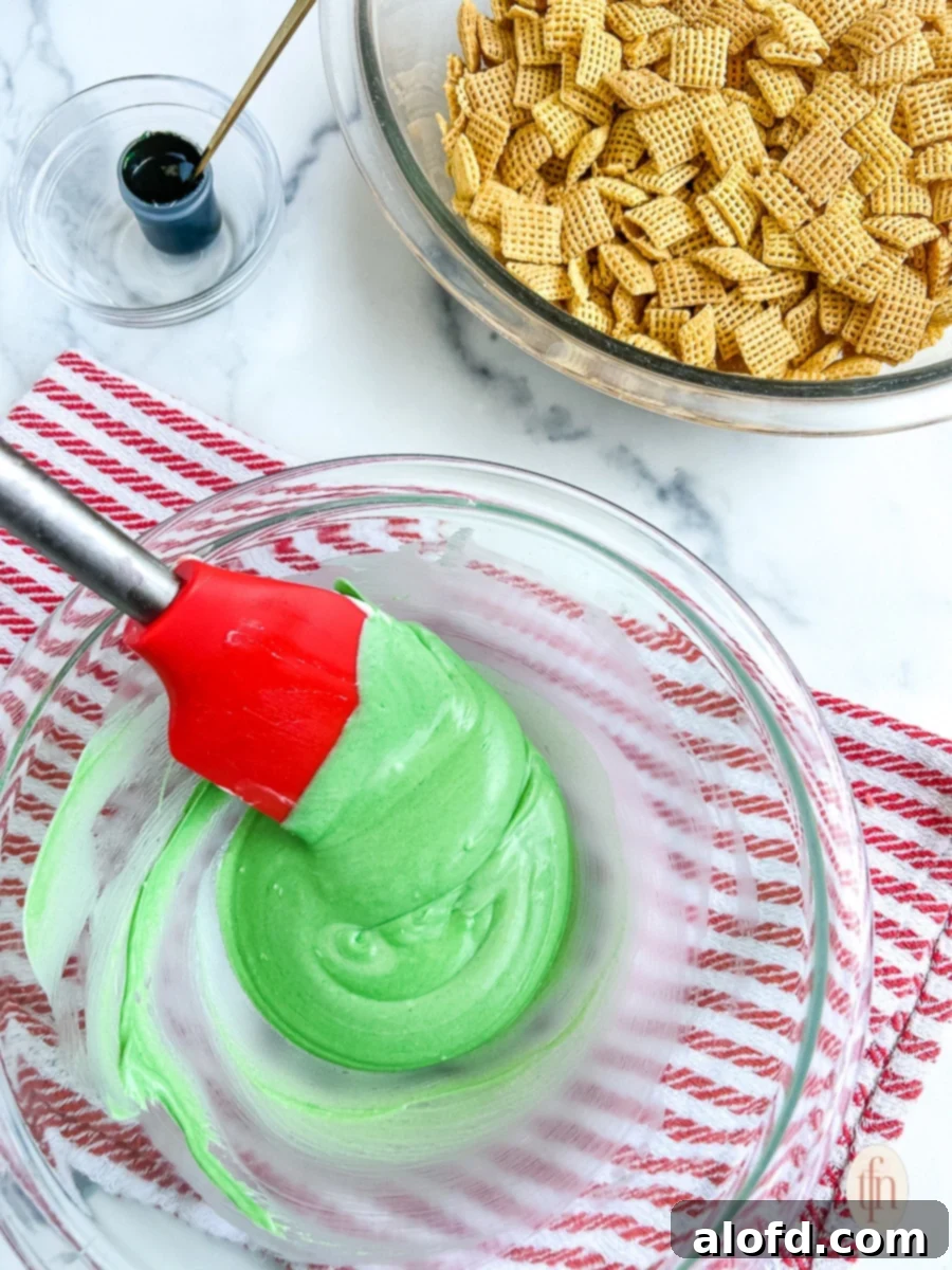 Festive Muddy Buddies 7 Glass bowl with green colored chocolate being stirred by a red rubber spatula.