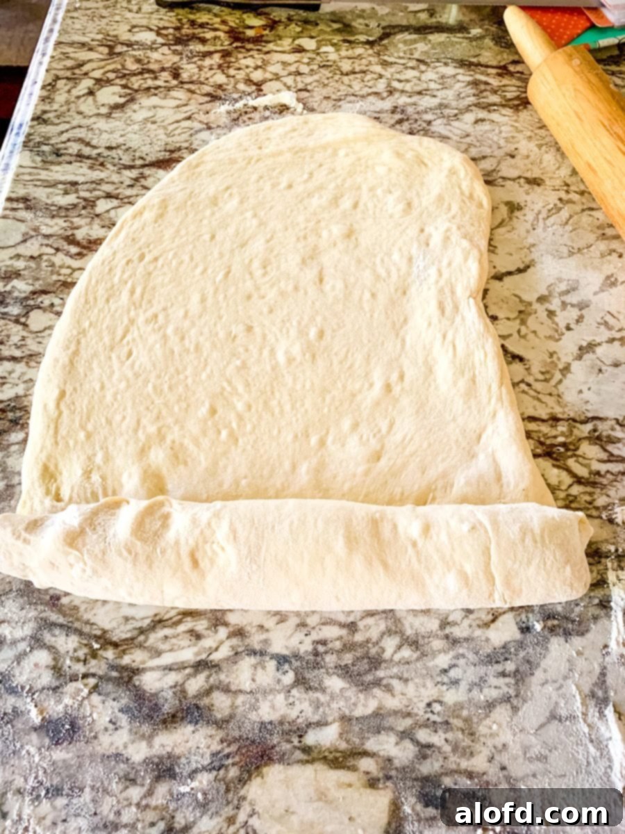 Homemade Fluffy Sandwich Bread 5 Hands rolling out yeast bread dough on a floured surface, preparing it for shaping into loaves.