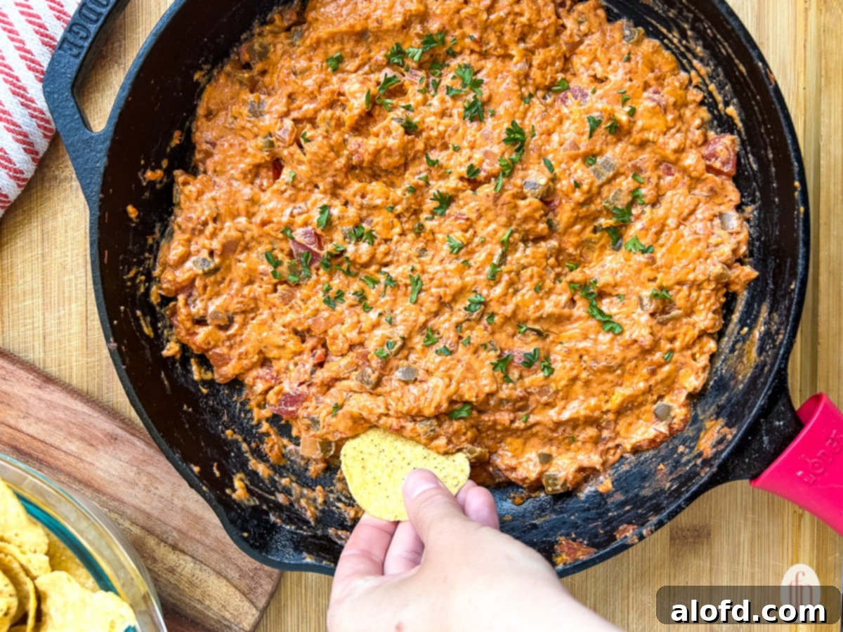 Woman dipping a chip into a cast iron skillet full of creamy, smoky salsa con queso.