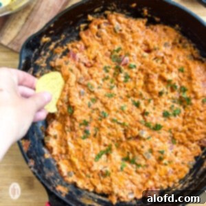 Dipping a tortilla chip into a cast iron skillet of smoked queso dip.