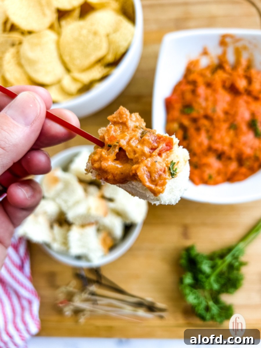 Large cube of bread on a toothpick, covered in smoked queso with chorizo, ready to be eaten.