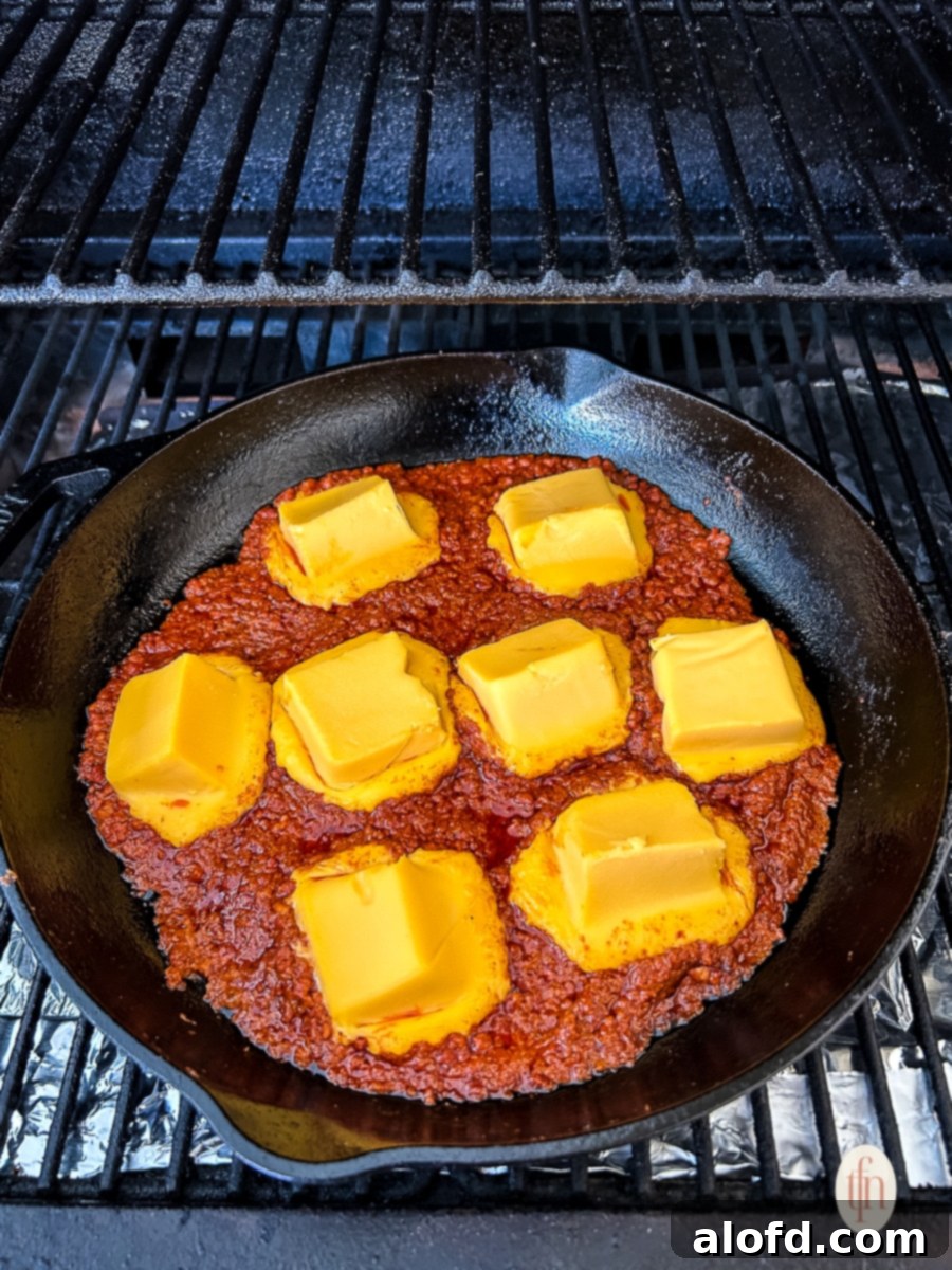 Large cubes of Velveeta cheese beginning to melt into the browned chorizo in a cast iron skillet.