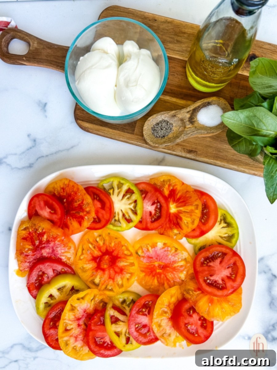 Platter of heirloom tomato slices next to bowls of white cheese and fresh basil for a caprese salad recipe.