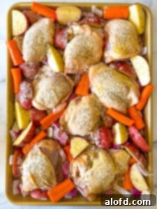 Jelly roll pan filled with seasoned, raw chicken thighs and chopped vegetables.