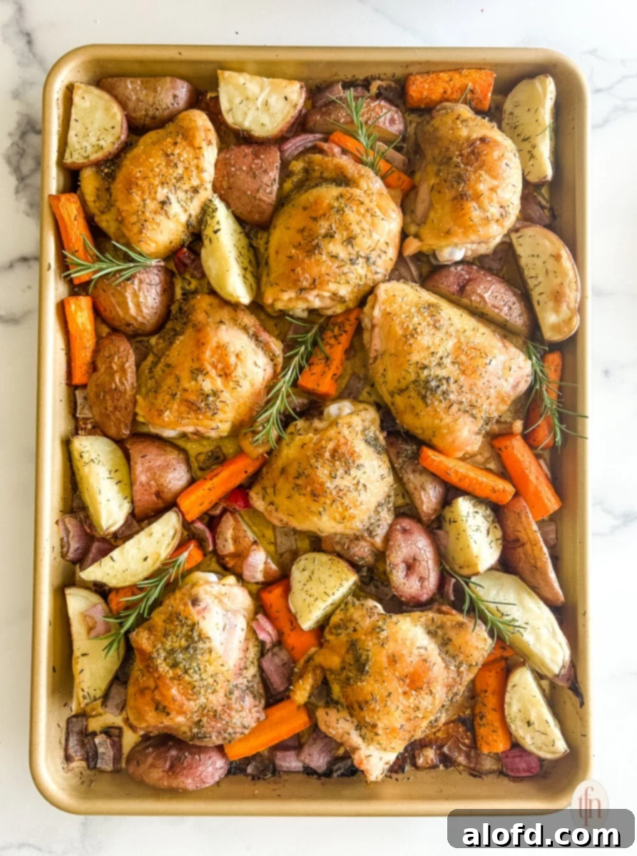 Close-up of boneless chicken thighs and colorful vegetables perfectly arranged on a sheet pan, ready for roasting.