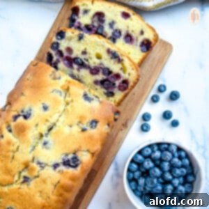 Luscious Blueberry Pound Cake 10 Blueberry pound cake on a cutting board next to a bowl of fresh blueberries.
