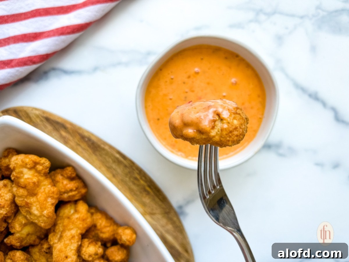 Dynamite Sweet Chili Sauce 3 A piece of fried food on a fork, generously dipped in orange-colored Bam Bam sauce.