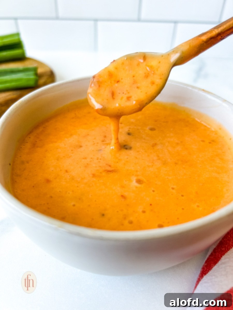 Dynamite Sweet Chili Sauce 4 Thick and creamy bang bang sauce dripping from a small spoon into a white bowl, showing its rich texture.