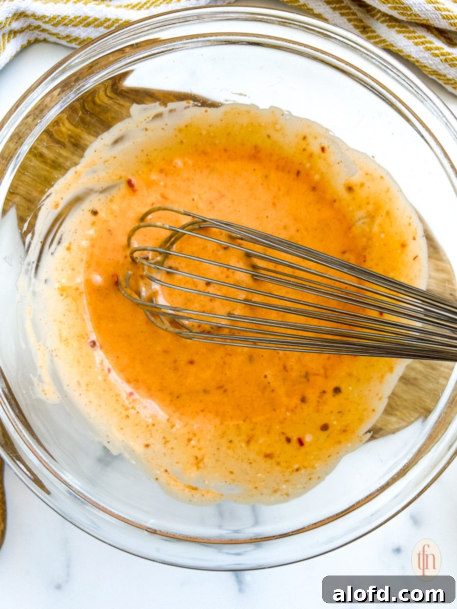 Dynamite Sweet Chili Sauce 7 Whisking shrimp sauce ingredients together in a glass mixing bowl, creating a smooth, orange-colored sauce.