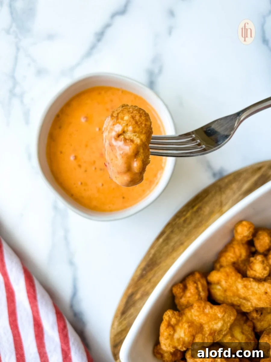 Dynamite Sweet Chili Sauce 8 Bang Bang shrimp covered with sauce, elegantly piled above a bowl containing more of the spicy condiment, ready to be served.