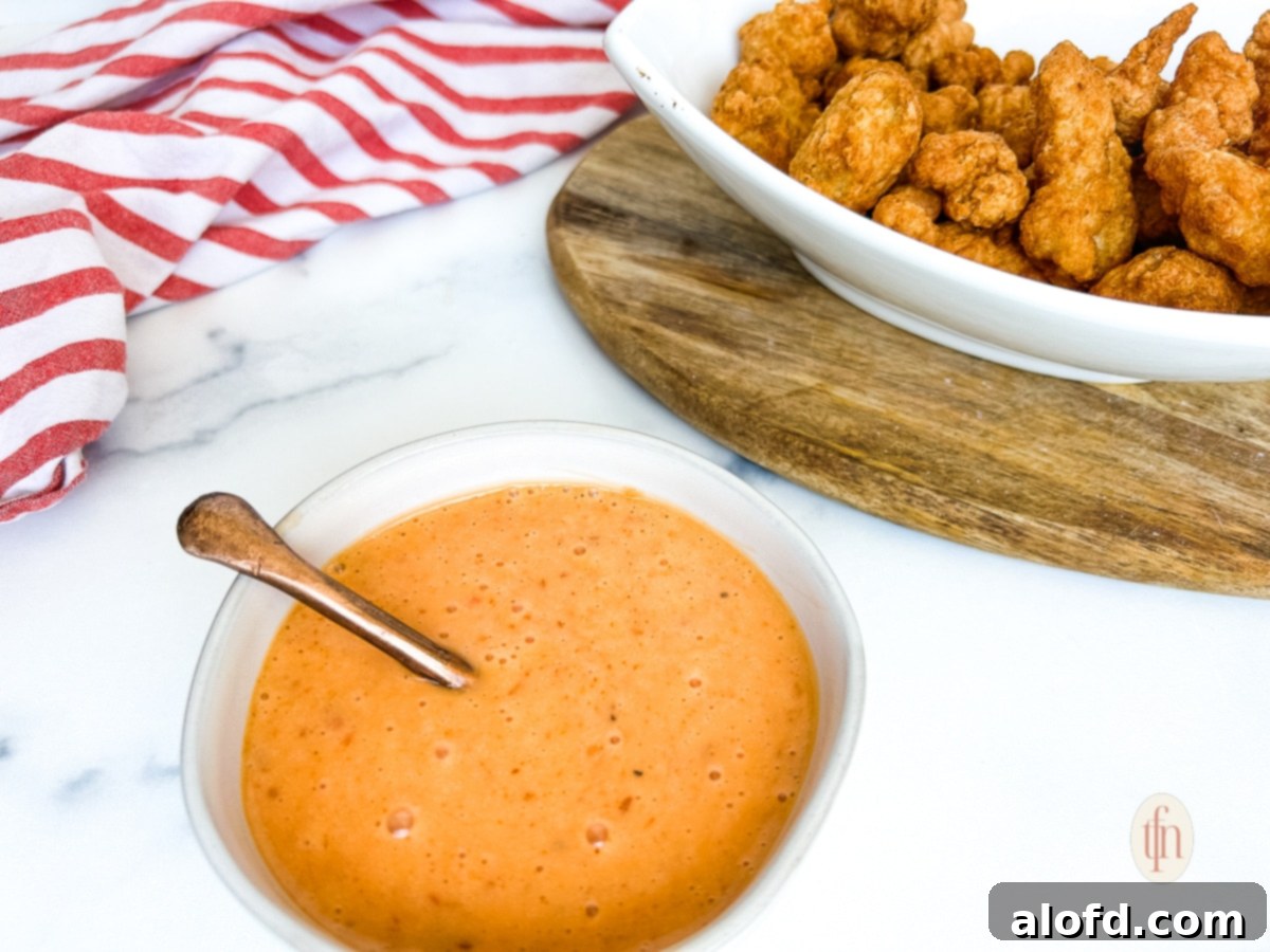 Dynamite Sweet Chili Sauce 9 A serving bowl of crispy fried chicken nuggets, with a small bowl of orange-colored Bang Bang sauce next to it for dipping.