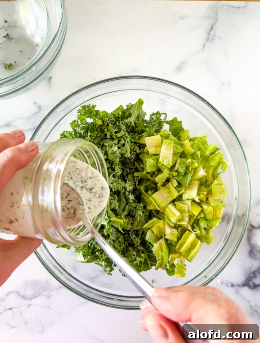 The Ultimate Green Goddess Salad 7 Pouring dressing over salad in a glass bowl.