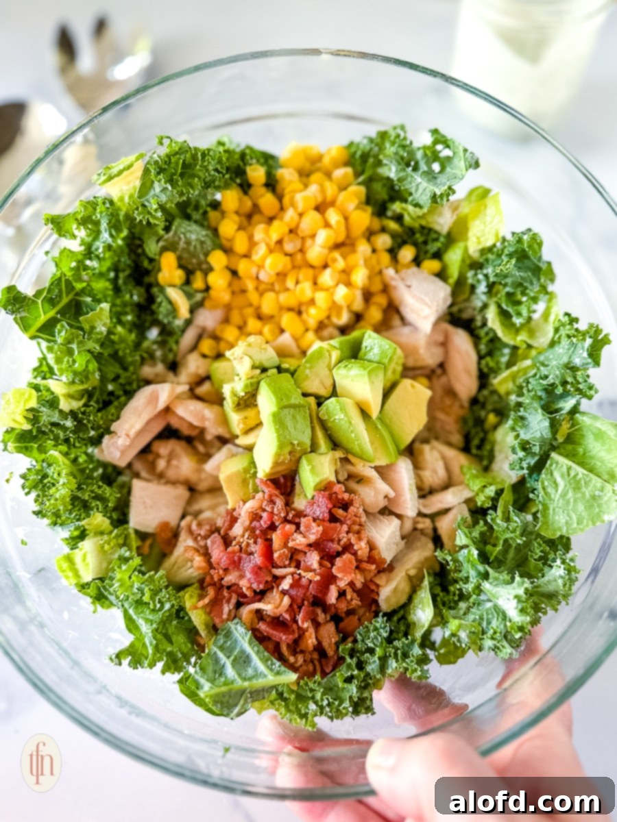 The Ultimate Green Goddess Salad 9 Holding glass bowl up filled with ingredients for a salad before they're mixed.