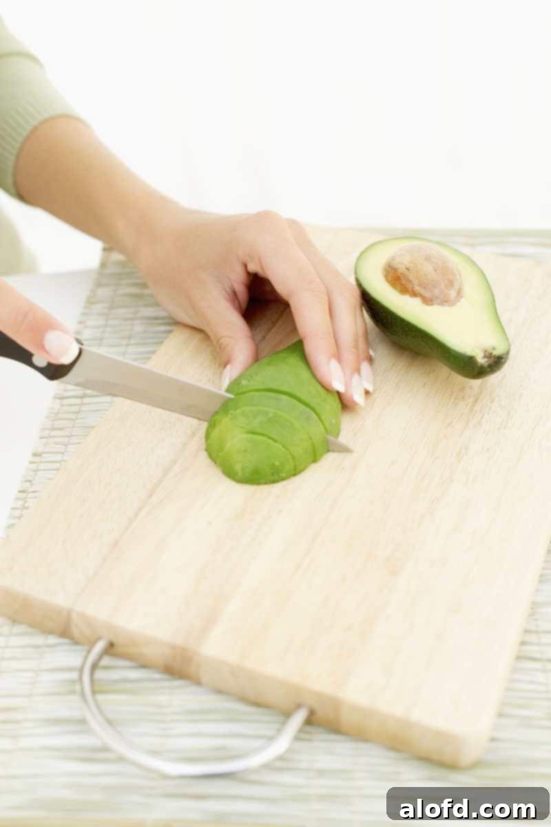 The Ultimate Green Goddess Salad 10 Hands slicing an avocado on a cutting board.