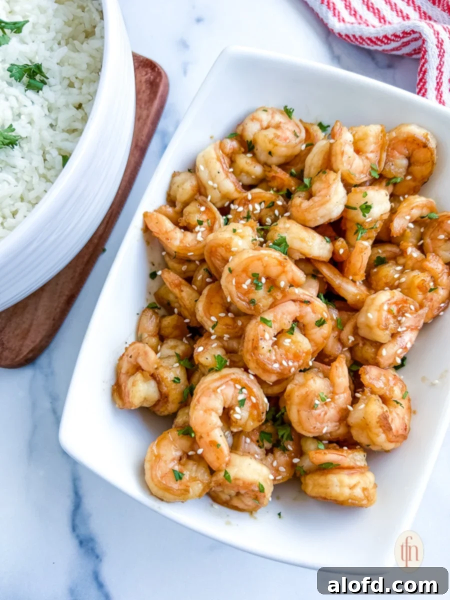 Blackstone hibachi shrimp on a white platter next to a bowl of white rice, perfectly cooked and ready to serve.