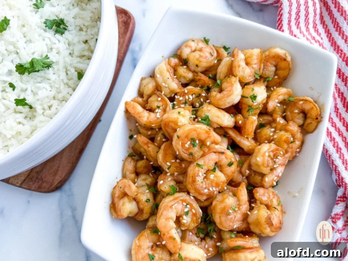 Blackstone hibachi shrimp arranged horizontally on a white platter next to a bowl of white rice, creating an inviting meal spread.