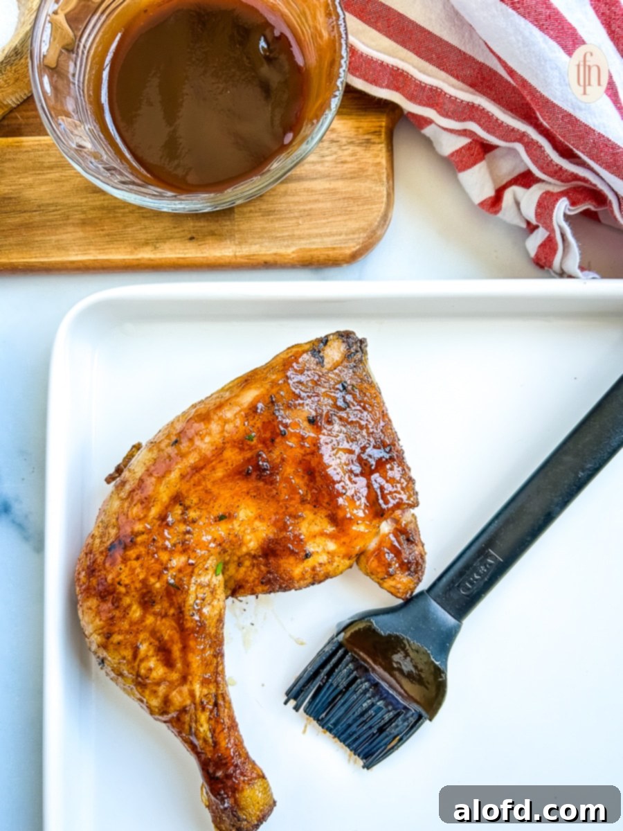 Juicy Smoked Chicken Drumsticks 8 A single perfectly smoked chicken quarter on a white plate, with a black silicone brush coated in barbecue sauce nearby, indicating a final glaze.