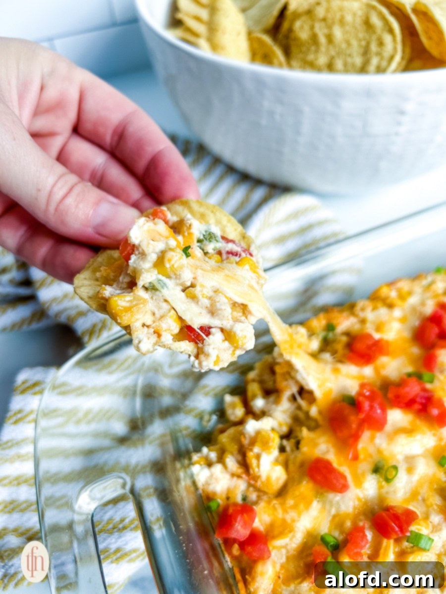 Crispy tortilla chip scooping up a generous portion of warm, cheesy corn dip from a baking dish.