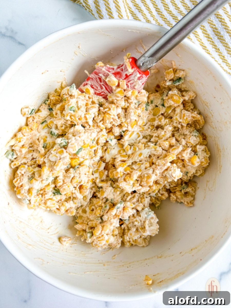 Mixing corn, cream cheese, and other ingredients in a large white bowl with a spatula.