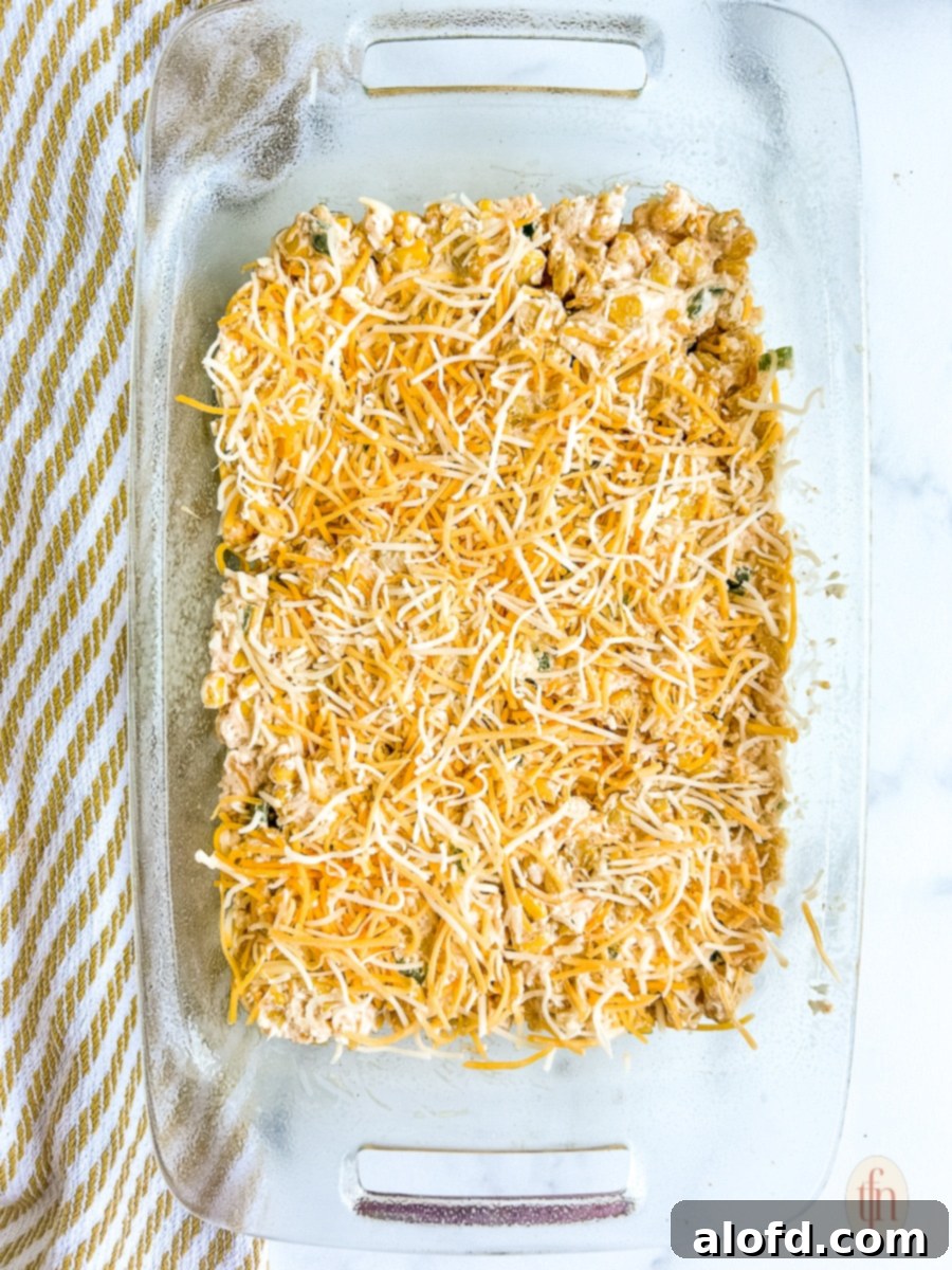 Baking dish with the prepared corn dip mixture, topped with an even layer of shredded cheese, ready for the oven.