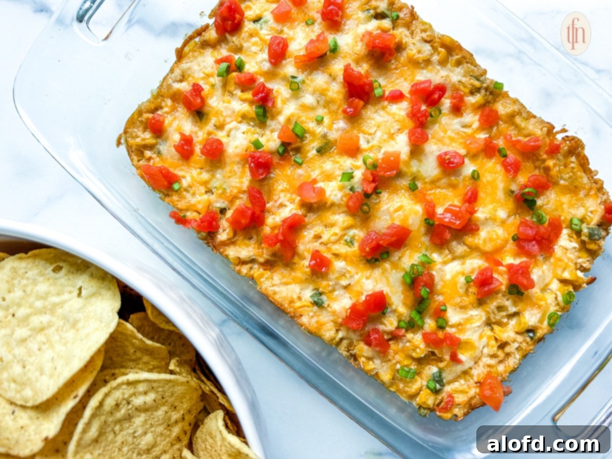 Another view of the warm cream cheese corn dip in a glass serving dish on a pristine white background, garnished and ready for serving.